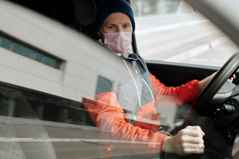 A man wearing a pink face mask is driving a vehicle