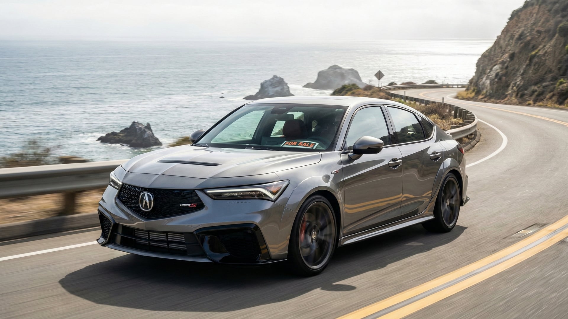 Gray Acura Integra sedan with a for sale sign driving along a coastal California highway.