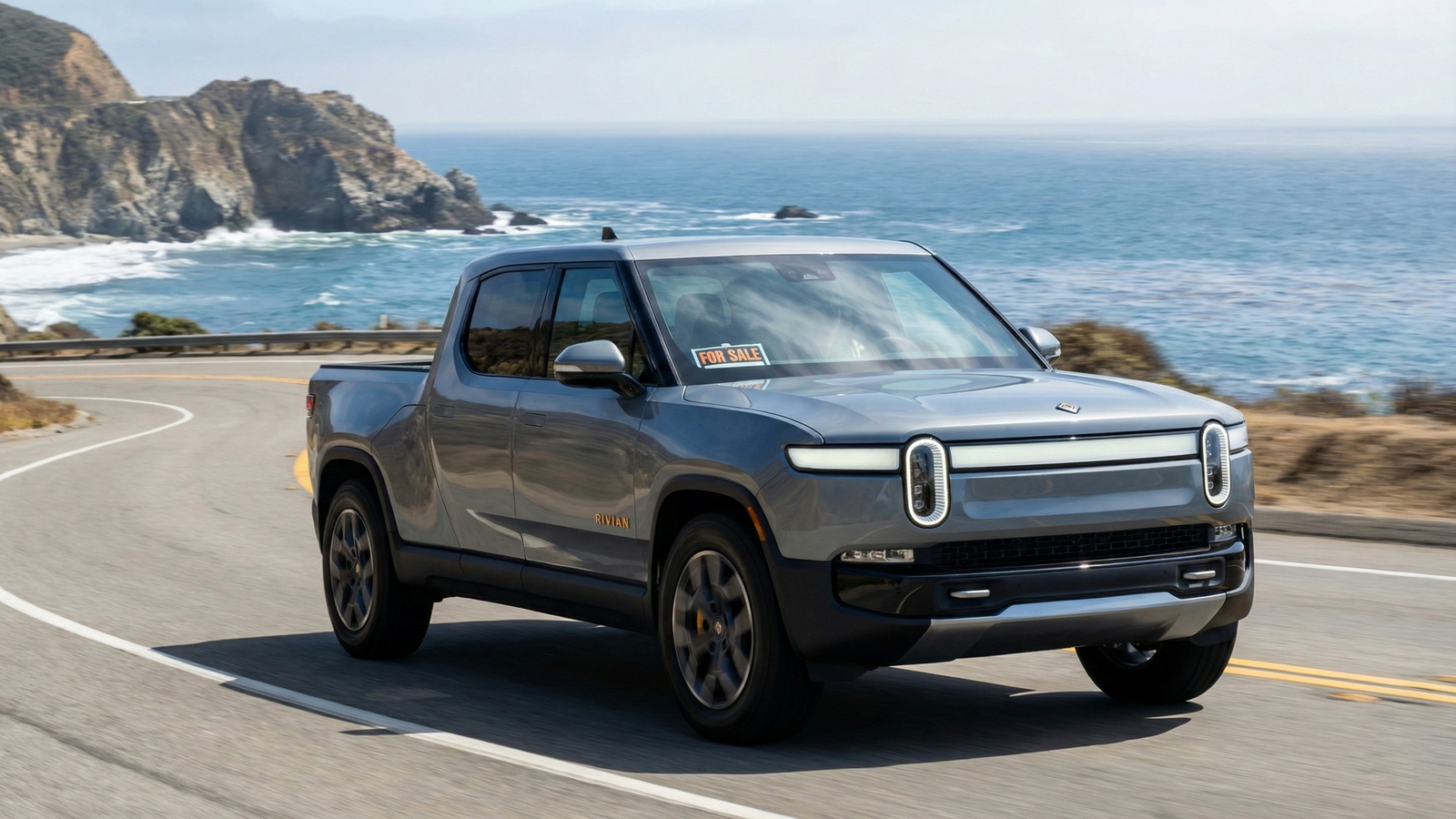 Sell Your Rivian R1T on the California Coast Gray Rivian R1T pickup with a for sale sign drives along a coastal California highway overlooking the ocean.