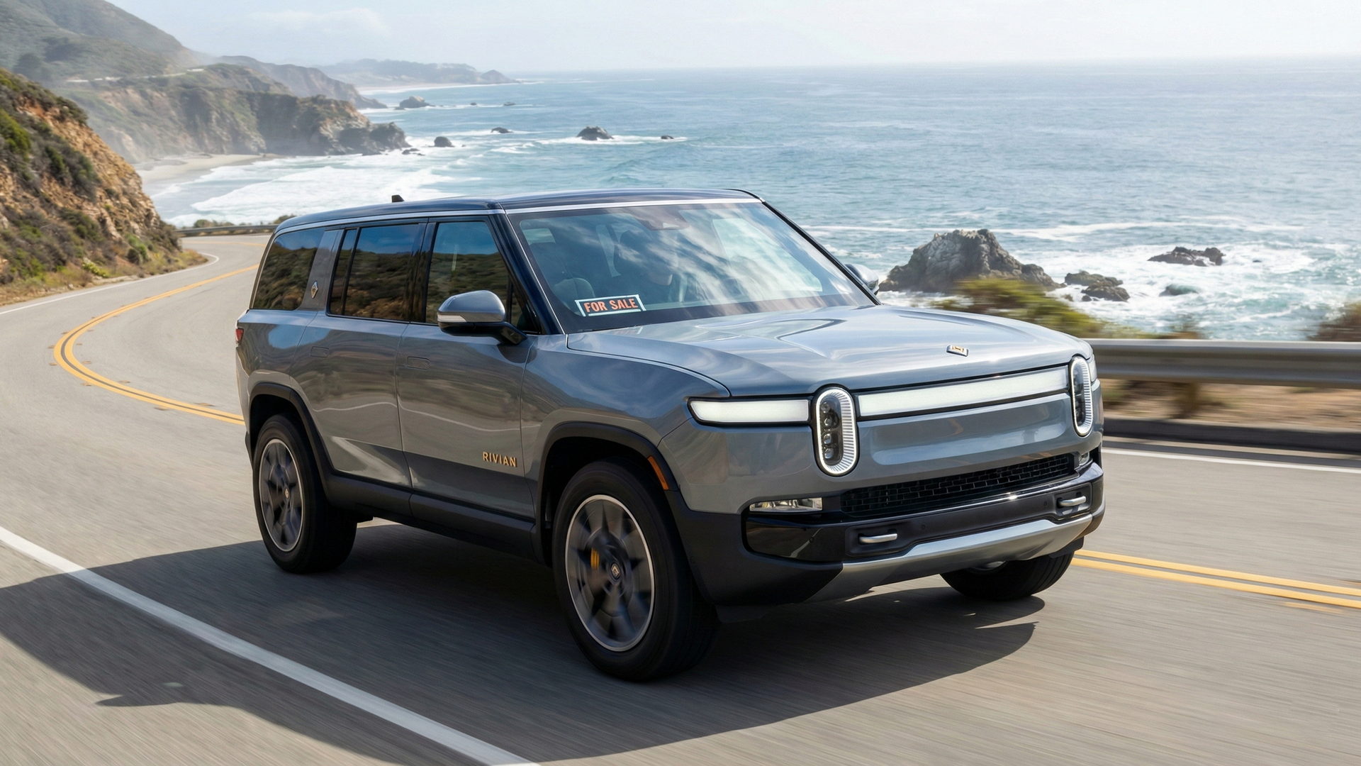 Sell Your Rivian R1S on the California Coast Gray Rivian R1S with a for sale sign driving along a coastal California highway.