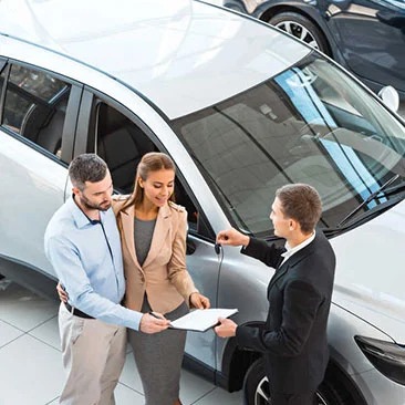Beat My Trade In Offer - Carzilo Best Cash Valuation A high-angle photo of a couple signing appraisal paperwork next to a silver SUV at a dealership, highlighting how Carzilo can beat my trade in offer.